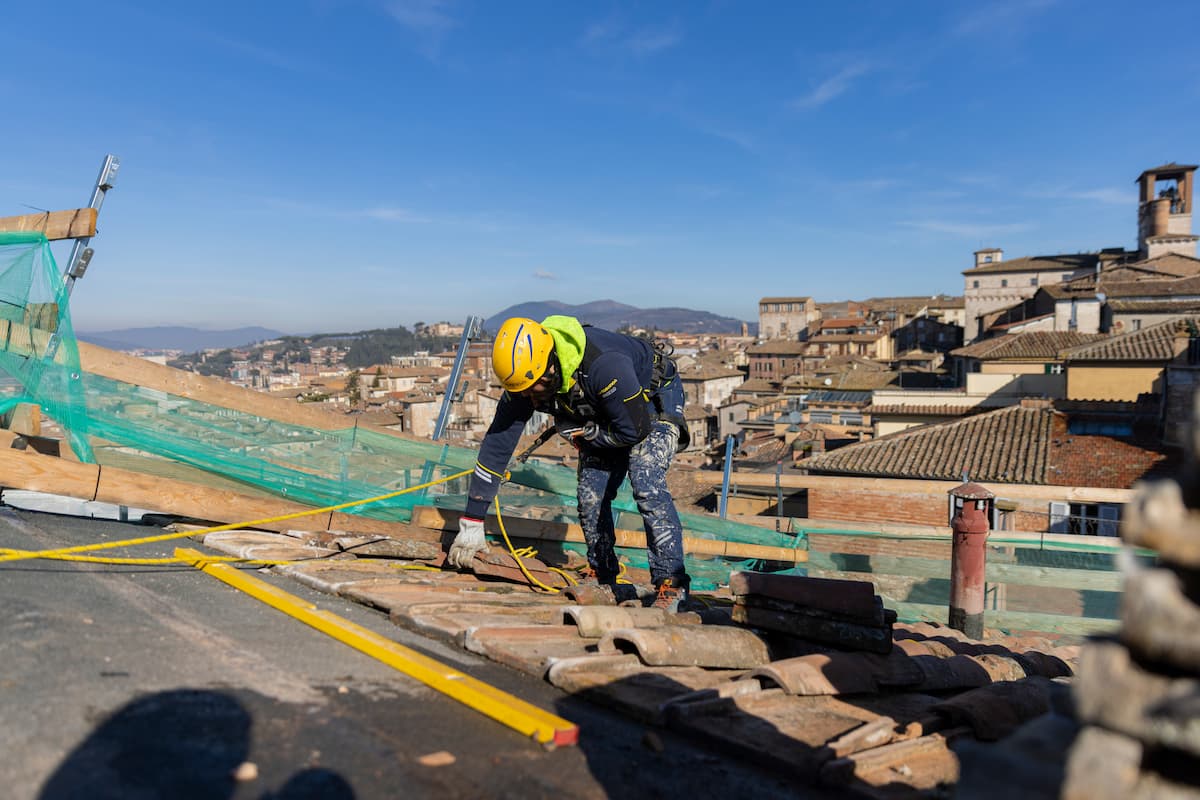 operaio Acrobatica su tetto a Perugia con in mano una tegola