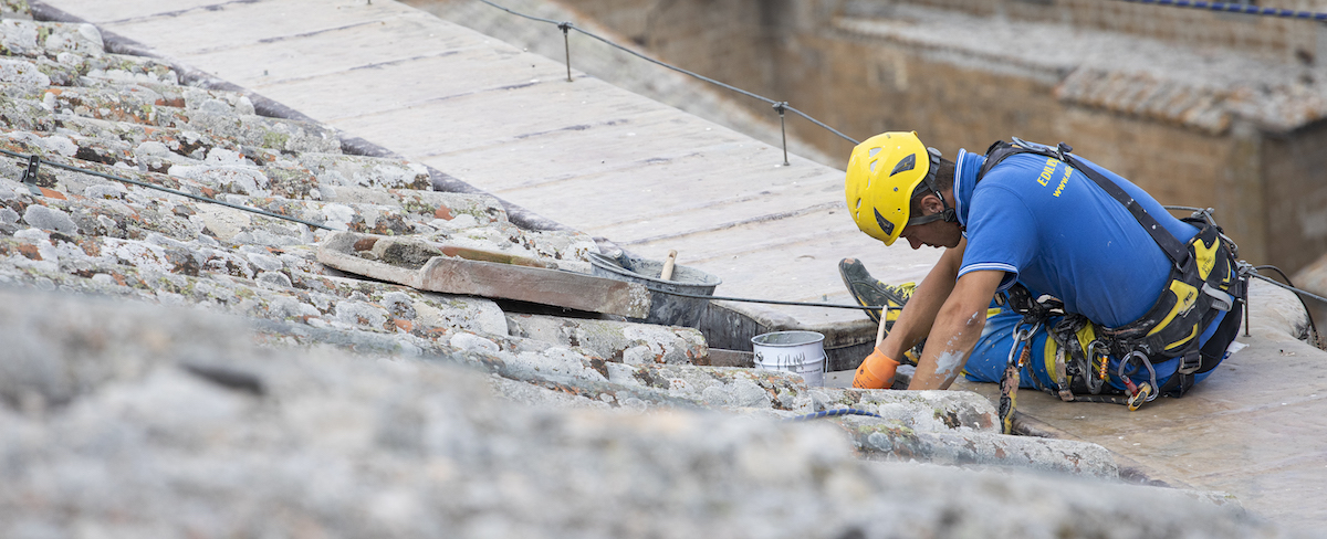 Muratore di Ediliziacrobatica che ristruttura un tetto fra le tegole 