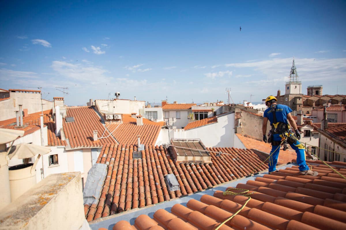 Tempistiche per il rifacimento del tetto: operaio di Acrobatica sui tetti che misura il tempo guardando il lavoro che ci sarà da fare